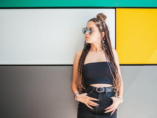 Charming teenage girl with dreadlocks in sunglasses nearby colorful wall
