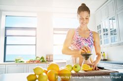 Muscular woman juicing an orange in her bright kitchen 0WDdW5