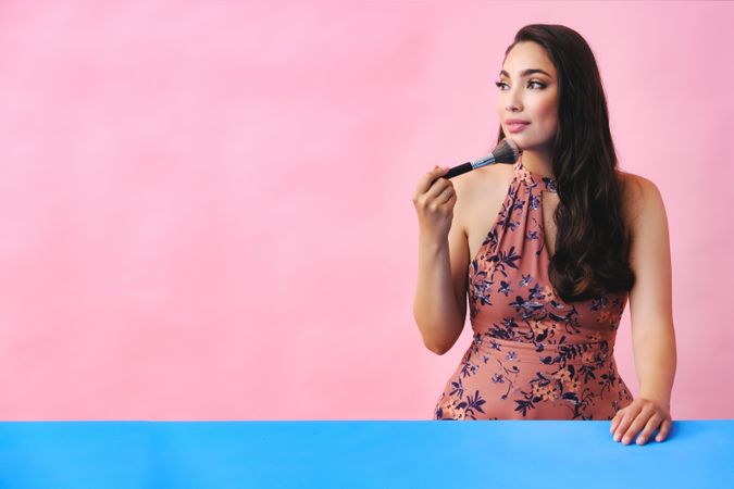 Hispanic woman with long brown hair holding large make up brush to her face, copy space