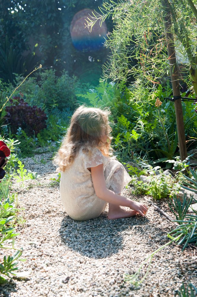 Side view of little girl sitting on pebble path in garden