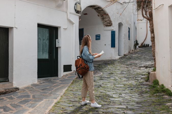 Side view of young woman holding a map looking up narrow street
