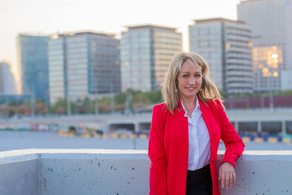 Woman smiling in red coat standing on top of building with view of city behind her