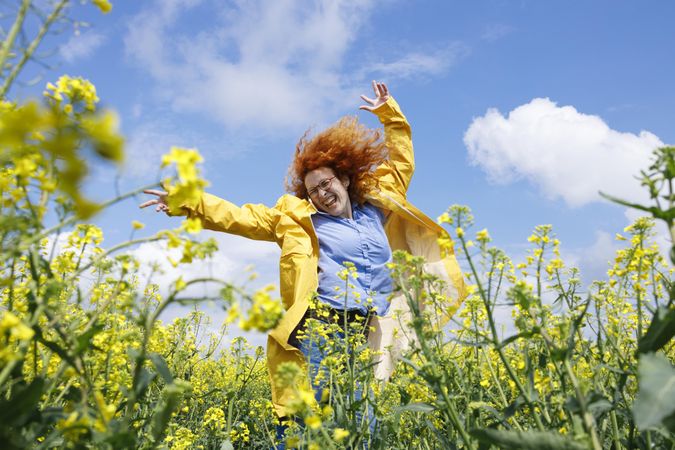Happy red haired woman dancing in a rapeseed field