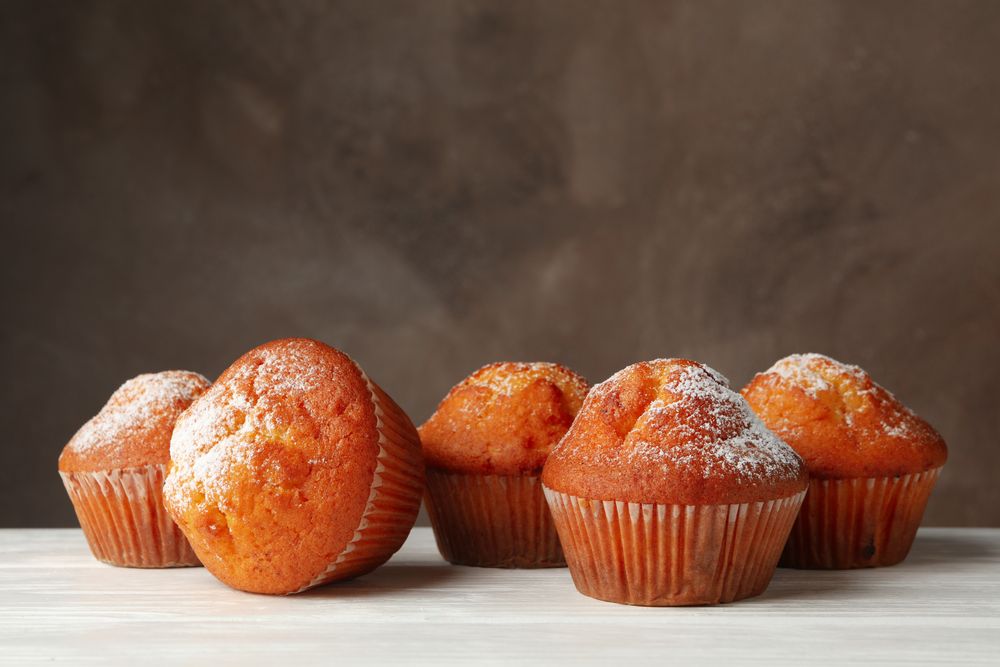 Tasty muffins on wooden table against brown background