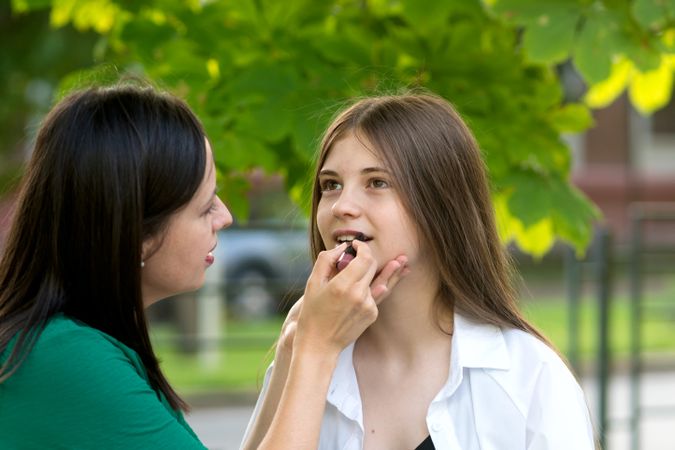 Mom applying lipstick to teenage daughter's lips