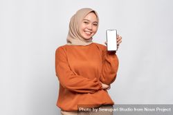 Confident Muslim woman smiling while holding up smart phone mock up 5nez20