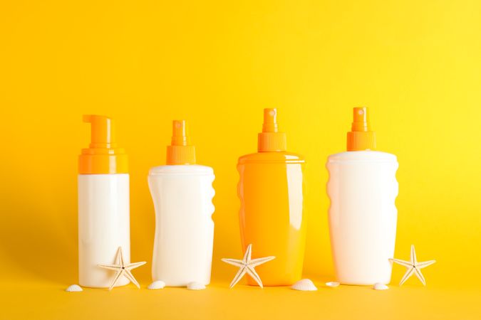 Sunscreen sprays with starfishes on color background, space for text. Safe tan accessories