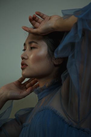 Side view of young woman in blue chiffon top touching her face