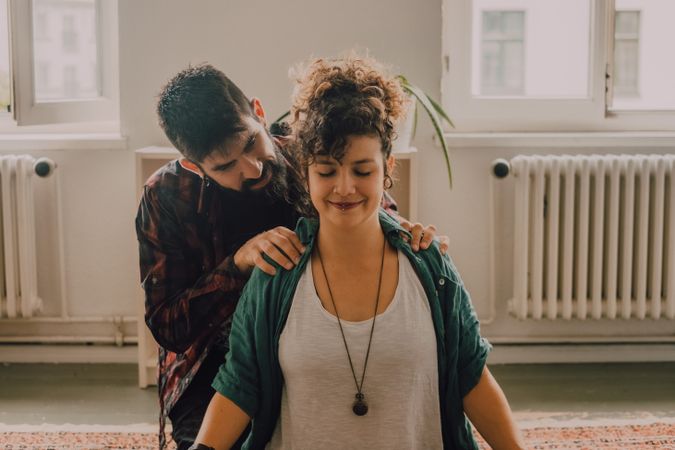 Man rubbing shoulders of joyful woman resting on floor at home
