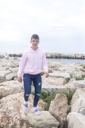 Young male teenager walking along rocky breakwater and looking at camera