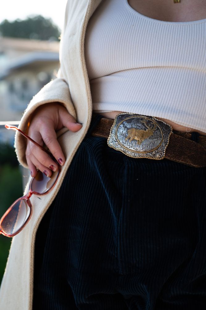 Cropped close up of woman holding sunglasses wearing vintage belt buckle