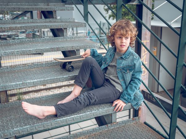 Preteen boy sitting on steps of staircase with skateboard