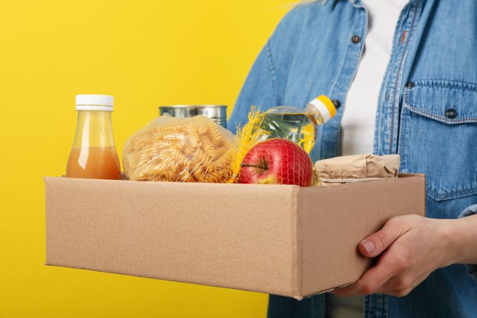 Woman holds donation box on yellow background. Volunteering