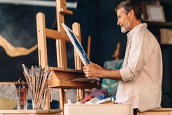 Older male painting taking his work off the easel