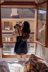 Young woman with cat near window and bed with waffles and drinks on tray