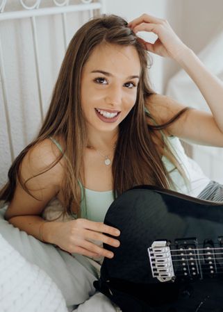 Young brunette woman playing guitar on bed
