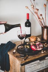 Rustic setting of hand pouring wine, cheese, long candles, with pomegranate, and dried poppies