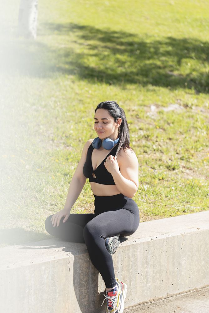 A young woman rests and relaxes with her eyes closed, sitting in the park, after exercising and playing sports
