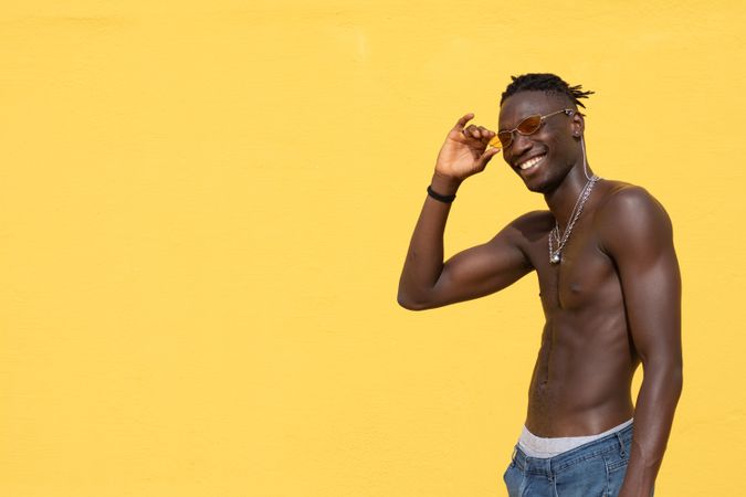 Cheerful Black man in trendy sunglasses posing near wall