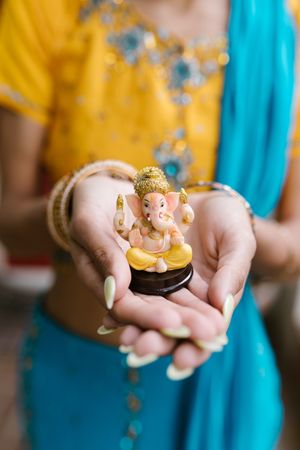 Cropped image of Indian woman wearing sari holding Ganesha figurine