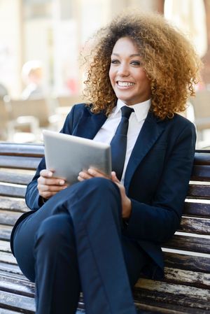 Happy woman in suit using her digital tablet on outdoor bench