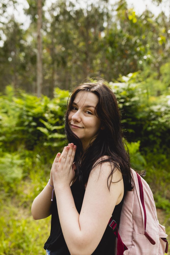 A young woman gestures her hands as if please, during a walk in a natural environment in summer