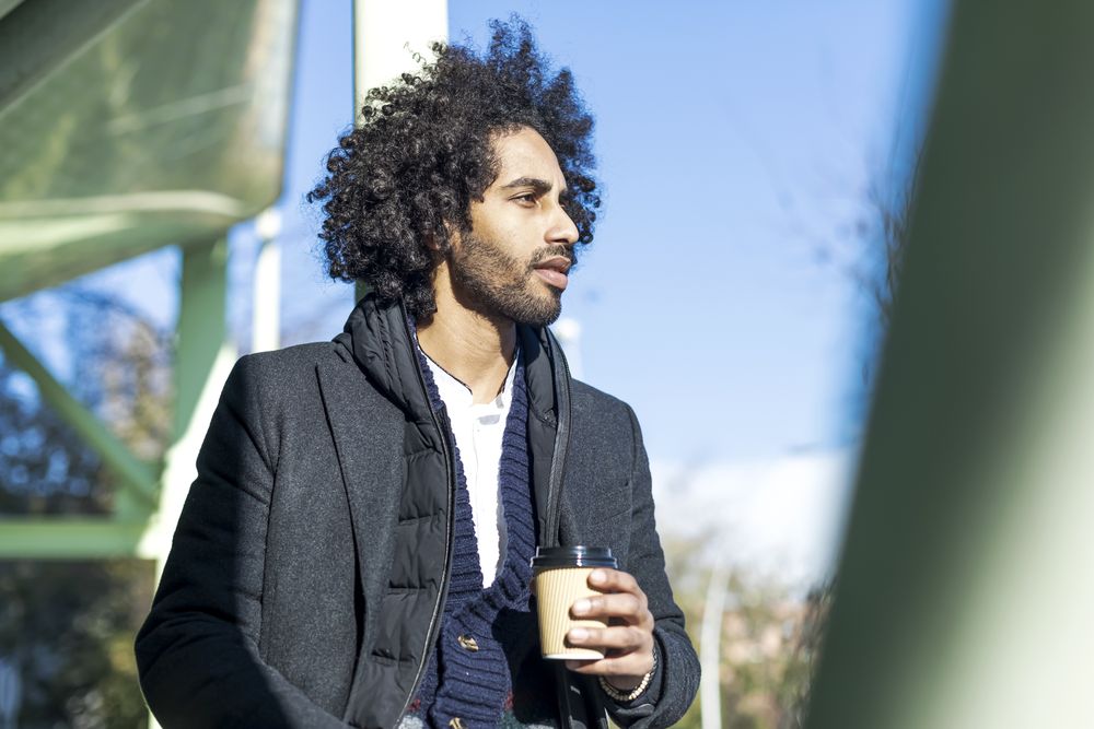 Black man in jacket holding beverage while looking in the distance
