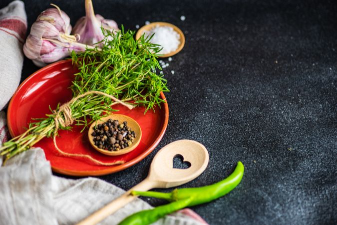 Pepper, herbs, oil and seasoning on red plate and kitchen towel on counter with copy space