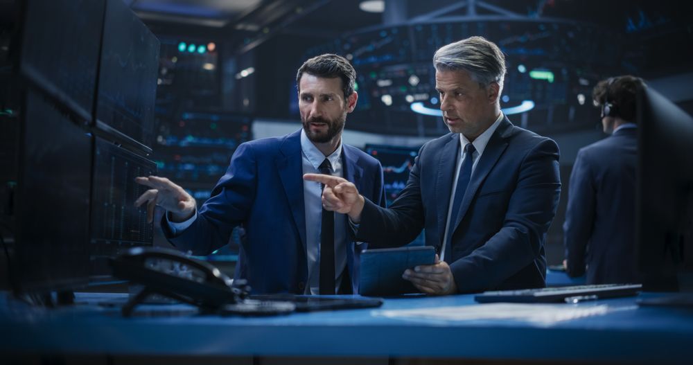 Two Successful Stock Exchange Brokers Using Tablet Computer, Talking About Asset Management Strategy for an International Business Client