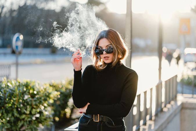 Stylish woman lighting cigarette near metro station