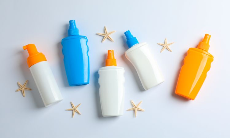 Flat lay composition with sunscreen sprays and starfishes on blank background, space for text. Summer vacation backdrop