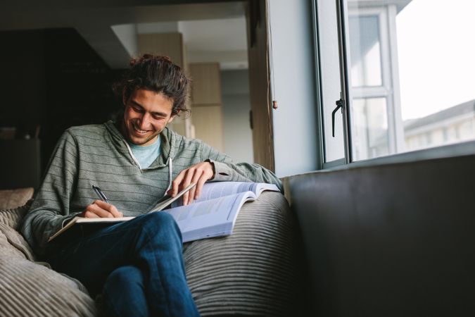 Smiling man sitting comfortably at home writing in a book