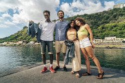 Portrait of a group of young diverse friends smiling at the camera on a pier by the sea.