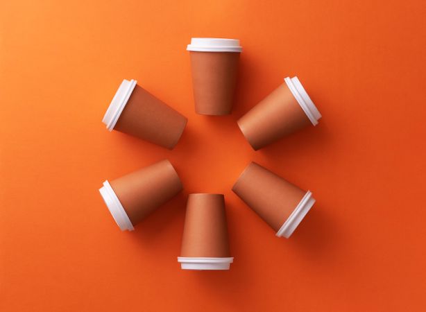 Disposable coffee cups on orange background in circle shape