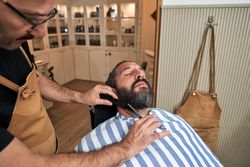 Barber cutting beard of client in barbershop