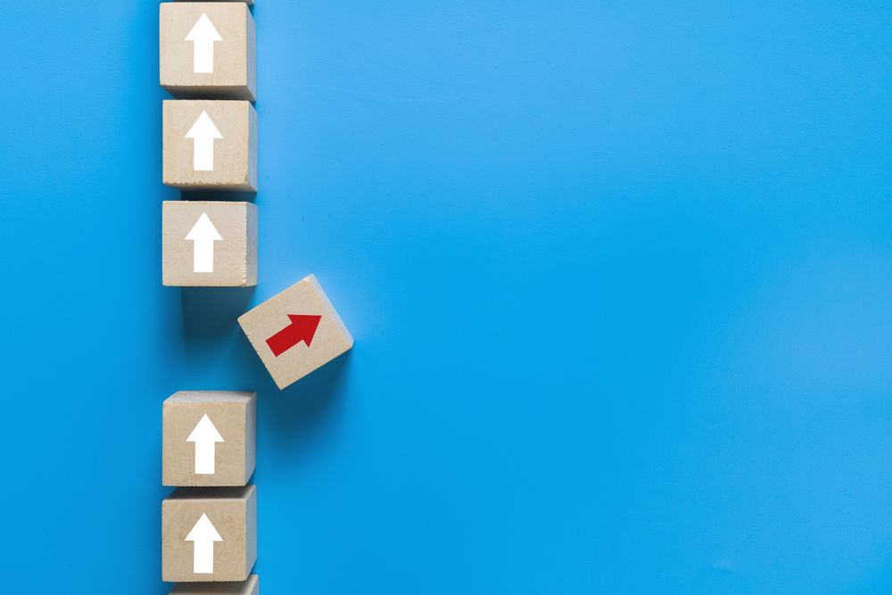 wooden blocks with up arrows and one different direction red arrow isolated on blue background. leadership concept