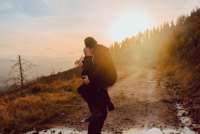 Smiling man holding cheerful guy on road on hill