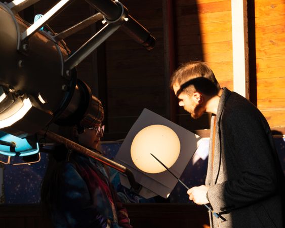 Man and girl examine projected solar image from telescope.