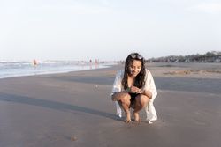 A young Hispanic woman is collecting seashells at the beach during sunset