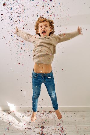 Happy preteen boy jumping and screaming with falling confetti