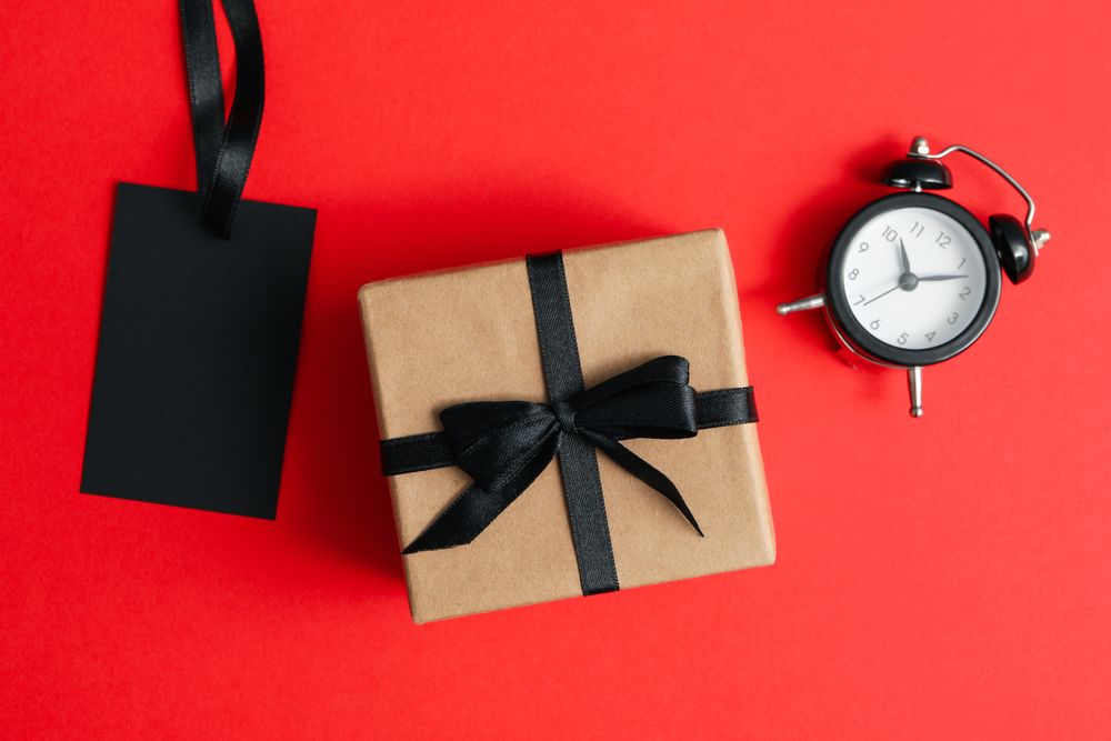 Alarm clock, gift box and tag on red background