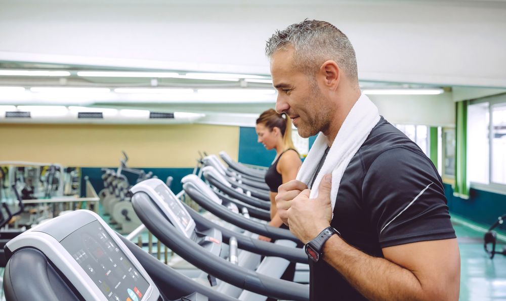 Side view of man with towel standing on treadmills on gym