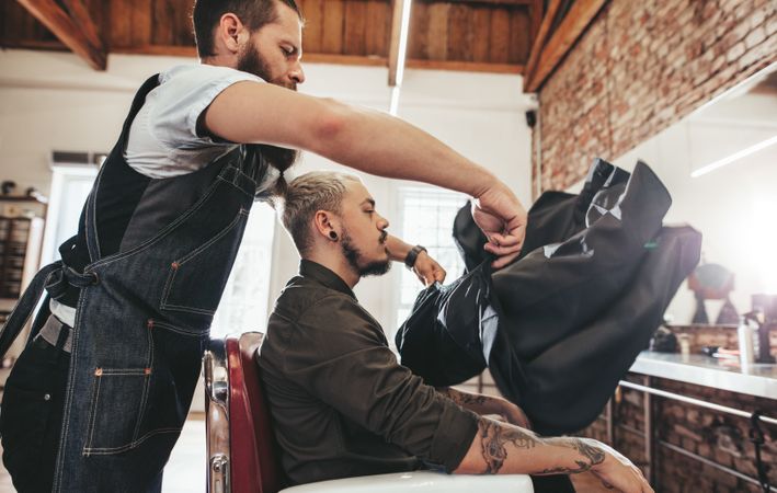 Barber putting salon cape on male client