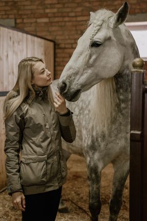 Woman hugging horse with long mane in face in stable