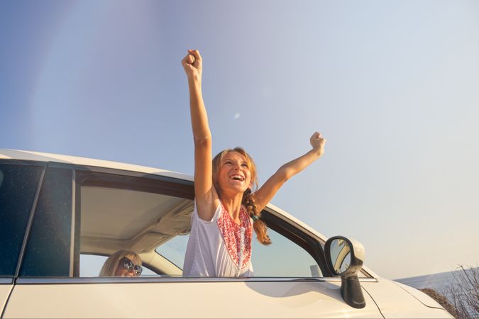 Blonde girl sticking her body out of the window of a car with th
