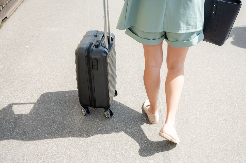 Crop woman with suitcase walking on street