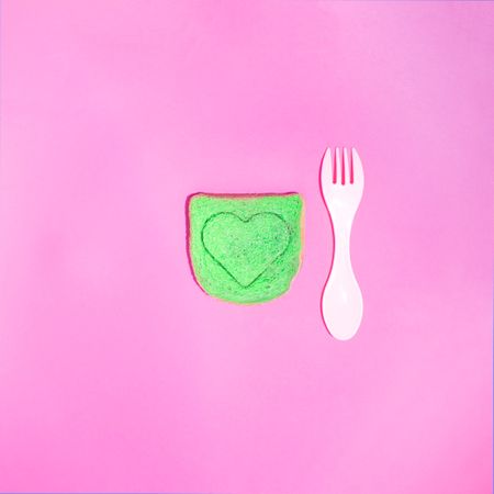 Green toast with heart in it on a pink background with fork
