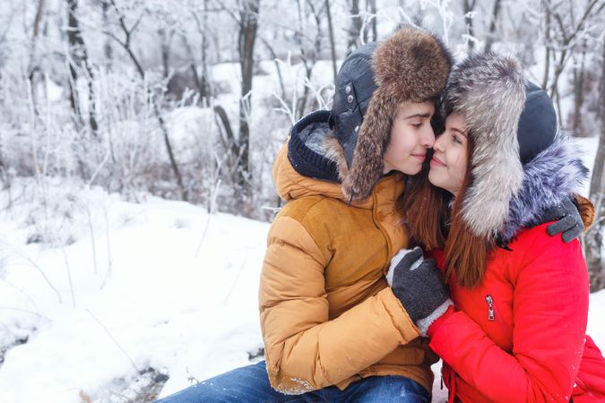 Affectionate teenage boy and girl sitting in snowy forest