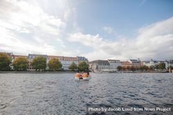 Wide shot of pedal boat on city river with European buildings behind 5aOLKb