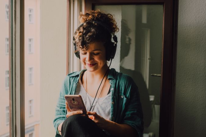 Cheerful woman in headphones using smartphone at home